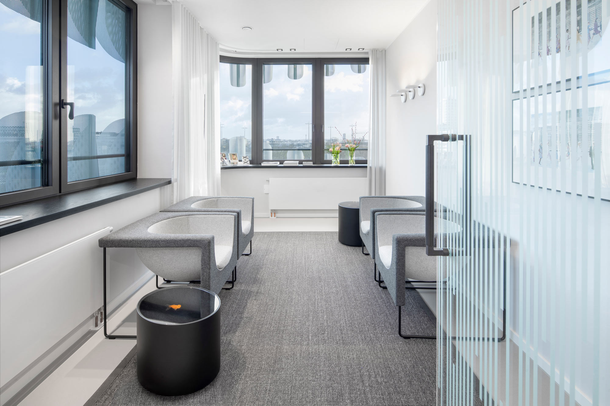 Fotografin fuer Chirurgen Fotos Schoenheitsklinik Chirurgie, ein Warteraum mit sehr stylischen Moebeln. Rechts im Bild ist eine Glastuer. Vorne und links sind Fenster, durch diese man sehr weit schauen kann.